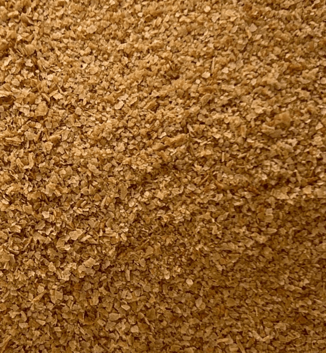 Close-up view of small, light brown wheat bran flakes with a coarse, textured appearance.